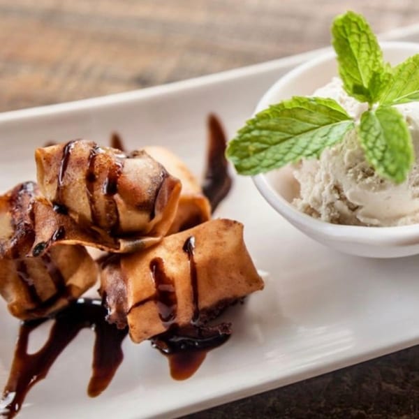 Fried banana spring rolls with chocolate drizzle and a scoop of vanilla ice cream with mint.