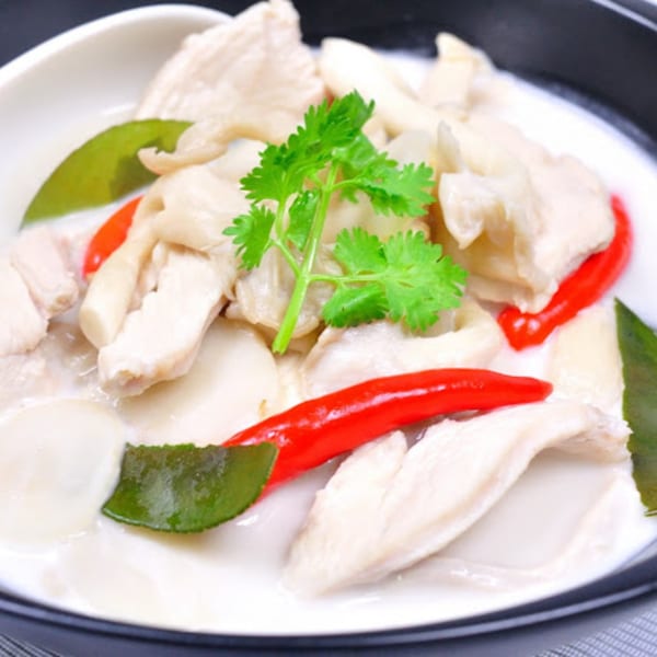 Creamy Tom Kha Gai soup with chicken, mushrooms, red chilies, and cilantro in a white bowl.