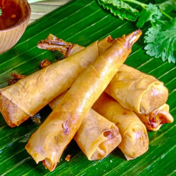 Crispy golden Mr. Thai spring rolls with shrimp tails, served on a banana leaf with dipping sauce.
