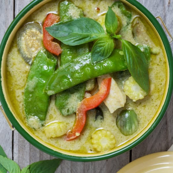 Close-up of Mr. Thai's green curry with vegetables, chicken, and basil in a green bowl.